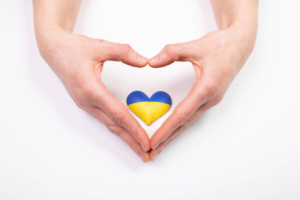 Флаг Украины в форме сердца в женских руках. Концепция солидарности с гражданами Украины.