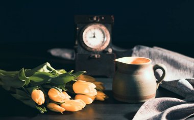 Eski bir sürahide sarı lale çiçeği buketi, karanlık arka planda ışık demeti. Sanat fotoğrafçılığı..
