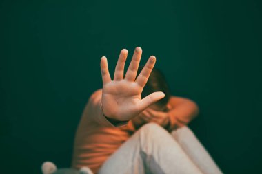 Çocuk şiddeti ve istismar konsepti. Küçük kız karanlık bir odada oturuyor, dur işareti gösteriyor.