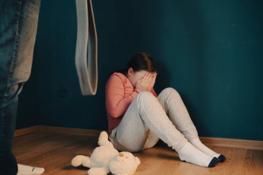 Çocuk istismarı, aile içi şiddet kavramı. Küçük kız yerde oturuyor ve bir yetişkinden korkuyor..