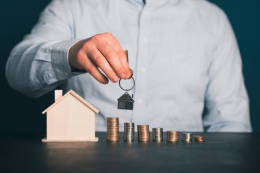 Emlakçının elinde bozuk para ve ev modelinin yanında anahtar var. Emlakçı, ipotek, evin, ev kredisi konsepti. Boşluğu kopyala