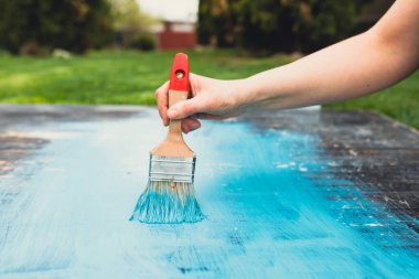 Kadının elindeki boya fırçası eski ahşabı mavi boyayla boyuyor. Yaratıcı tasarım, ev yenileme teması, DIY konsepti