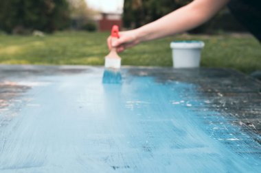 Kadının elindeki boya fırçası eski ahşabı mavi boyayla boyuyor. Yaratıcı tasarım, ev yenileme teması, DIY konsepti
