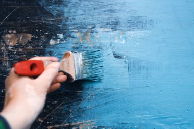 Kadının elindeki boya fırçası eski ahşabı mavi boyayla boyuyor. Yaratıcı tasarım, ev yenileme teması, DIY konsepti
