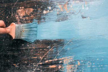 Kadının elindeki boya fırçası eski ahşabı mavi boyayla boyuyor. Yaratıcı tasarım, ev yenileme teması, DIY konsepti