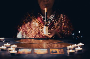 Falcı elinde mumların yanındaki masada tarot kartlarıyla. Tarot kartları kristal kürenin üzerine yayılmış. Tahmin konsepti..
