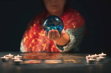 Falcı elinde mumların yanındaki masada tarot kartlarıyla. Tarot kartları kristal kürenin üzerine yayılmış. Tahmin konsepti..