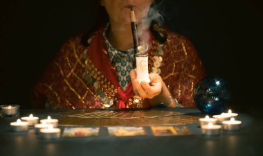 Falcı elinde mumların yanındaki masada tarot kartlarıyla. Tarot kartları kristal kürenin üzerine yayılmış. Tahmin konsepti..