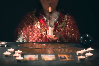 Falcı elinde mumların yanındaki masada tarot kartlarıyla. Tarot kartları kristal kürenin üzerine yayılmış. Tahmin konsepti..