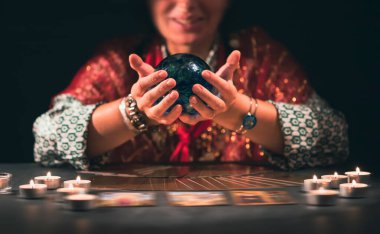 Falcı elinde mumların yanındaki masada tarot kartlarıyla. Tarot kartları kristal kürenin üzerine yayılmış. Tahmin konsepti..