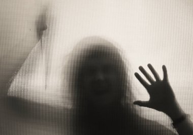 Korku, cadılar bayramı arkaplanı, camın arkasında elinde bıçak tutan karanlık bir figür.