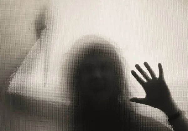 Korku, cadılar bayramı arkaplanı, camın arkasında elinde bıçak tutan karanlık bir figür.