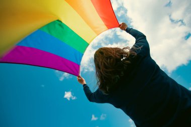 Yeşil çayırda oturan bir kadın elinde Eşcinsel Gökkuşağı Bayrağı' yla. Biseksüel, gey, lezbiyen, transseksüel sembol. Aynı cinsiyetli çiftler için mutluluk, özgürlük ve aşk kavramı