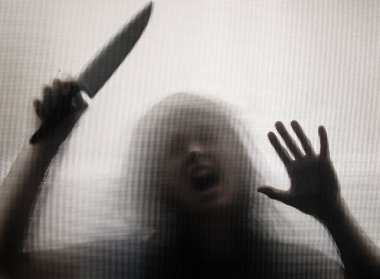 Korku, cadılar bayramı arkaplanı, camın arkasında elinde bıçak tutan karanlık bir figür.