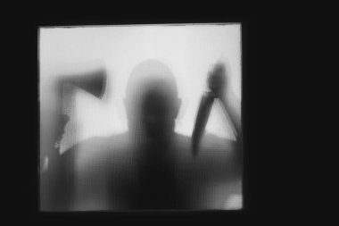 Korku, cadılar bayramı arkaplanı, elinde balta ve bıçak tutan bir adamın camının arkasındaki gölgeli figür.