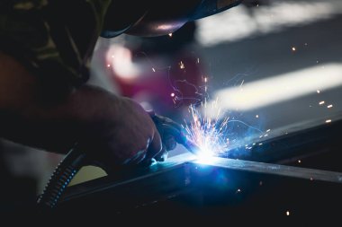 Etrafındaki kıvılcımlar uçuşurken tamirci atölyesinde kaynak ve öğütme yapıyordu. Koruyucu kask ve ekipman takıyor..