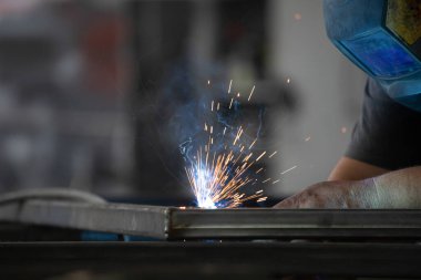 Etrafındaki kıvılcımlar uçuşurken tamirci atölyesinde kaynak ve öğütme yapıyordu. Koruyucu kask ve ekipman takıyor..