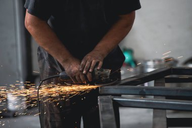Profesyonel kumaş işçisi, endüstriyel atölyedeki elektrikli öğütücüyle çalışma masasında metal profili kesiyor..
