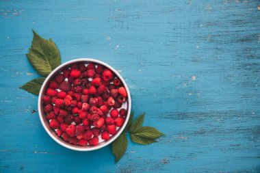 Turkuaz ahşap arka planda bir kase taze kırmızı ahududu..