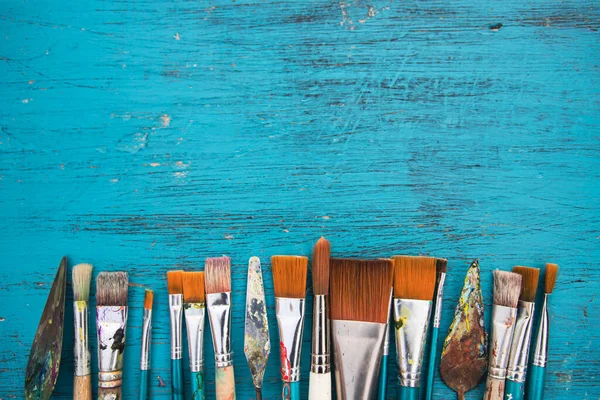 Artistic art supply utensils with paintbrushes on turquoise wooden background with copy space. Flat lay photo