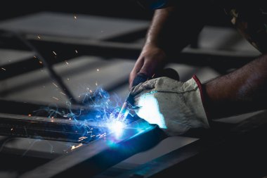 Handyman performing welding and grinding at his workplace in the workshop, while the sparks 