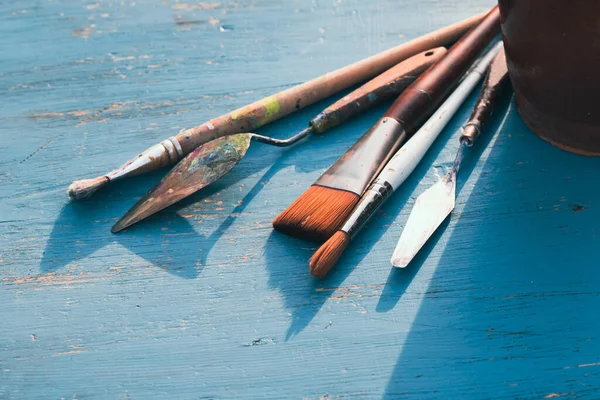 Artistic art supply utensils with paintbrushes on turquoise wooden background with copy space.
