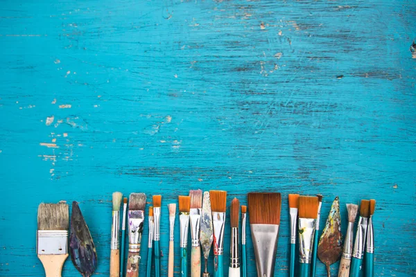 Artistic art supply utensils with paintbrushes on turquoise wooden background with copy space. Flat lay photo