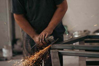 Profesyonel kumaş işçisi, endüstriyel atölyedeki elektrikli öğütücüyle çalışma masasında metal profili kesiyor..