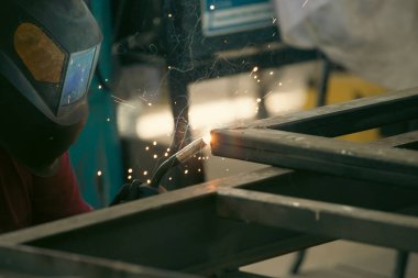 Etrafındaki kıvılcımlar uçuşurken tamirci atölyesinde kaynak ve öğütme yapıyordu. Koruyucu kask ve ekipman takıyor..