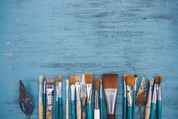 Artistic art supply utensils with paintbrushes on turquoise wooden background with copy space. Flat lay photo