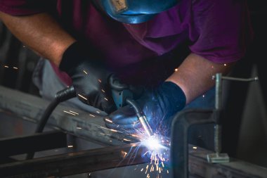 Handyman performing welding and grinding at his workplace in the workshop, while the sparks 