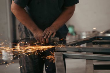 Profesional fabric worker cutting metal profile on the work table with an electric grinder in the industrial workshop.