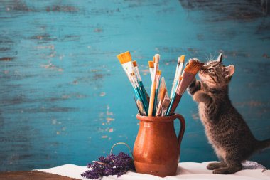 Still life of paint brushes  in clay jug, lavender flowers and a cute kitten on vintage turquoise background