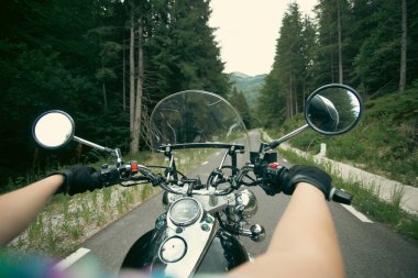 Orman yolunda giden motosikletli bir sürücünün ellerinde. Seyahat ve spor, hız ve özgürlük kavramı