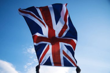 Mavi gökyüzüne karşı bir adamın ellerinde sallanan İngiltere bayrağı. Arkadan bak. Büyük Britanya, zafer ve başarı
