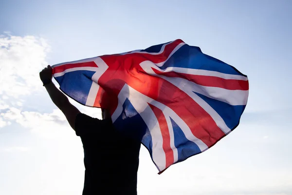 The flag of England waving in the hands of a man against the blue sky. View from the back. Great Britain, victory and success