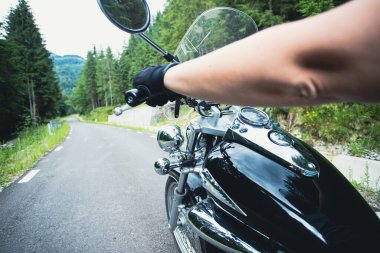 Orman yolunda giden motosikletli bir sürücünün ellerinde. Seyahat ve spor, hız ve özgürlük kavramı