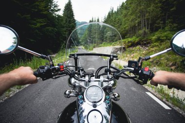 Orman yolunda giden motosikletli bir sürücünün ellerinde. Seyahat ve spor, hız ve özgürlük kavramı