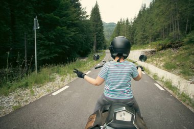 Biker girl on a motorcycle on summer forest road. Travel and sport, speed and freedom concept.