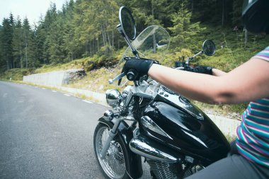 Close-up on the hands of a motorcycle driver riding on forest road. Travel and sport, speed and freedom concept