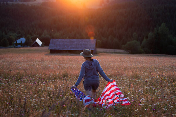 Young woman holding american USA flag in the sunset. Independence Day or traveling in America concept. 