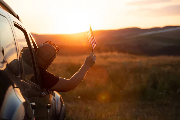 Man holding an American flag on a road trip. Independence Day or traveling in America concept.