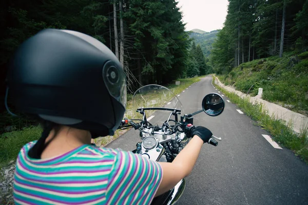 Biker girl on a motorcycle on summer forest road. Travel and sport, speed and freedom concept.