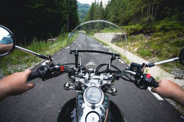 Close-up on the hands of a motorcycle driver riding on forest road. Travel and sport, speed and freedom concept