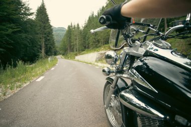Close-up on the hands of a motorcycle driver riding on forest road. Travel and sport, speed and freedom concept
