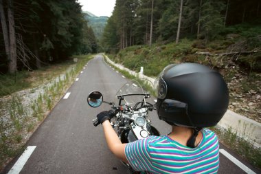 Biker girl on a motorcycle on summer forest road. Travel and sport, speed and freedom concept.