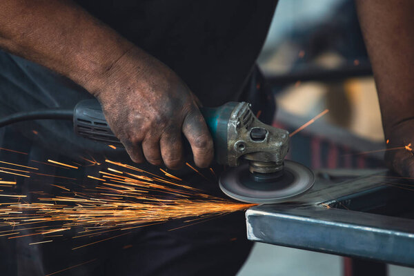 Profesional fabric worker cutting metal profile on the work table with an electric grinder in the industrial workshop.