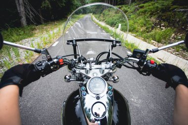Close-up on the hands of a motorcycle driver riding on forest road. Travel and sport, speed and freedom concept