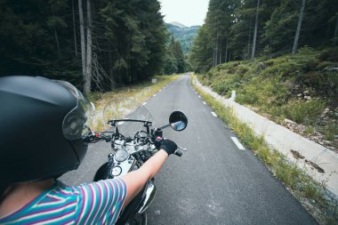 Biker girl on a motorcycle on summer forest road. Travel and sport, speed and freedom concept.