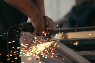 Profesyonel kumaş işçisi, endüstriyel atölyedeki elektrikli öğütücüyle çalışma masasında metal profili kesiyor..